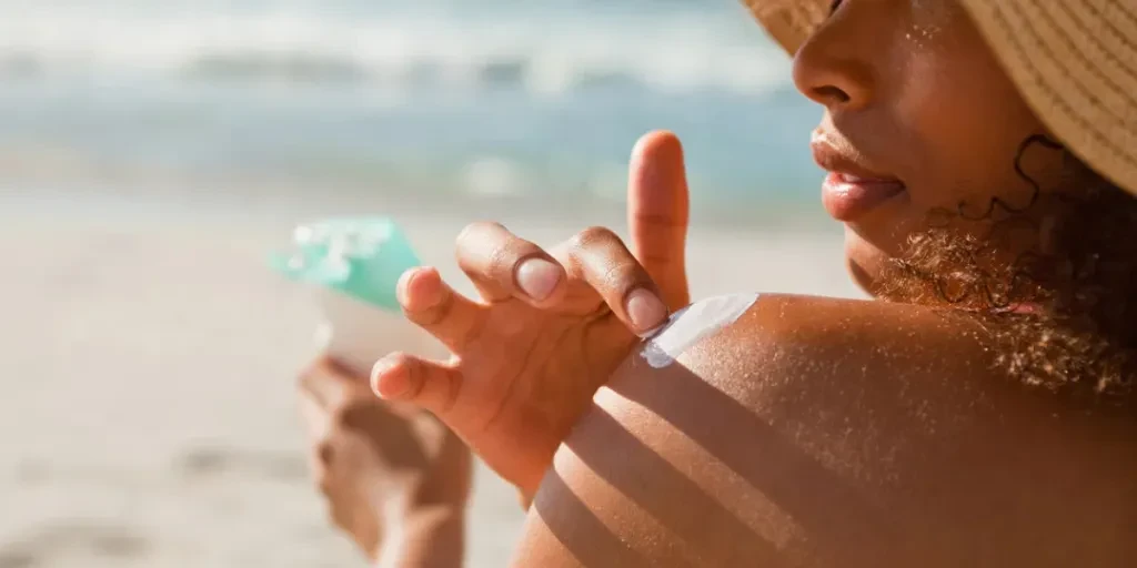 Young woman applying sunscreen on her shoulder while sitting on the beach