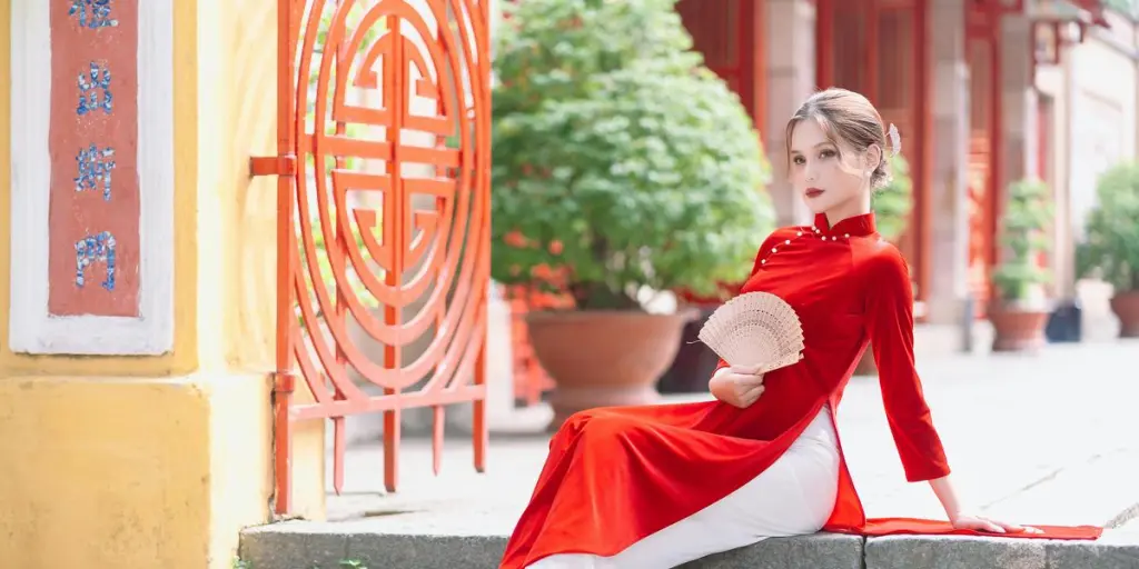 Young woman in a red qipao, holding a fan, poses gracefully on steps