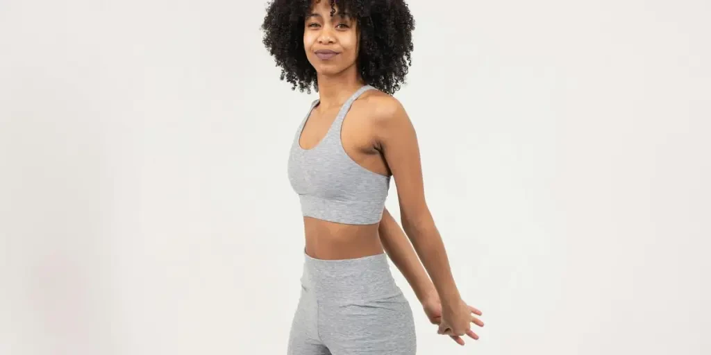 Young woman with curly hair stretching in sportswear on a white background