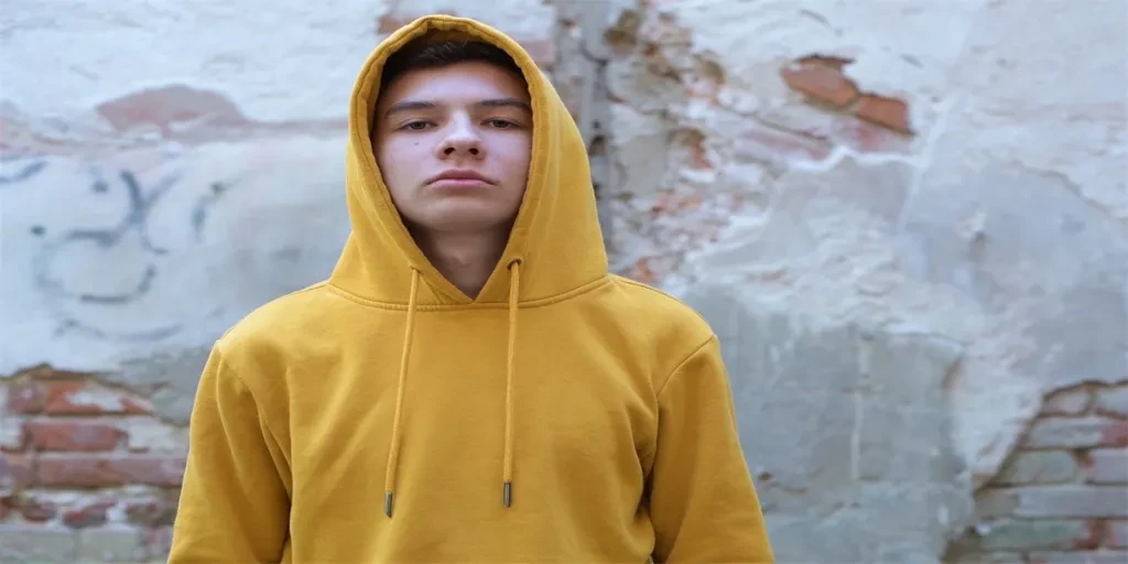 a teenager in a yellow hoody arrogantly looks at the camera, against the background of a decrepit wall of an old building