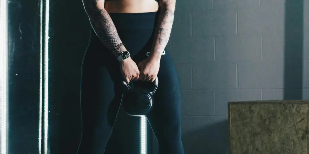 a woman with tattoos holding a kettle in a gym