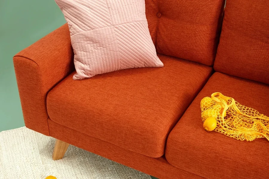 An orange sofa with a pink pillow and fake lemons