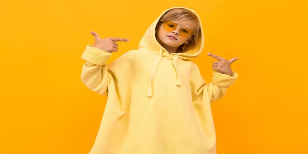 blond boy with a panama in a light hoodie with glasses posing on a orange studio background