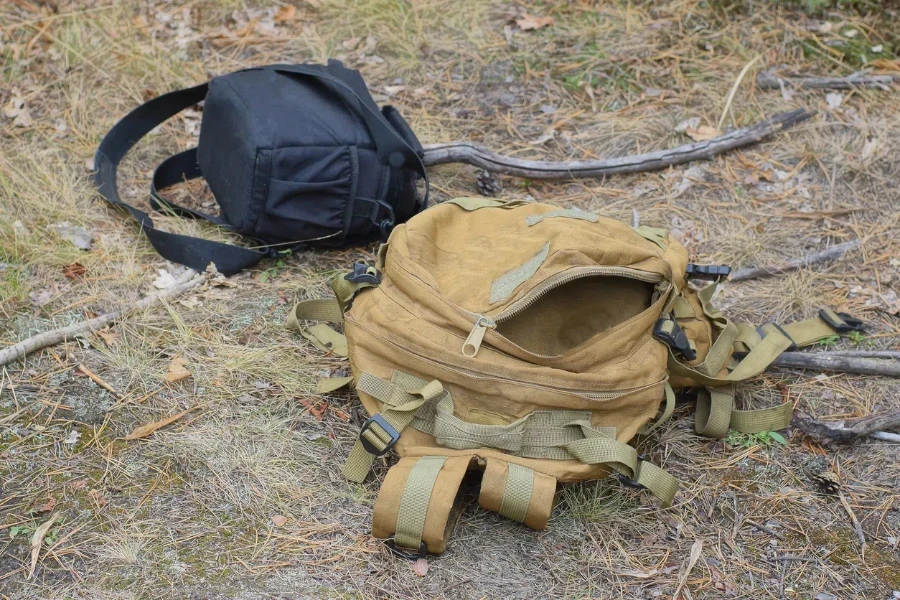 brown army backpack and black bag lie on gray ground on summer street