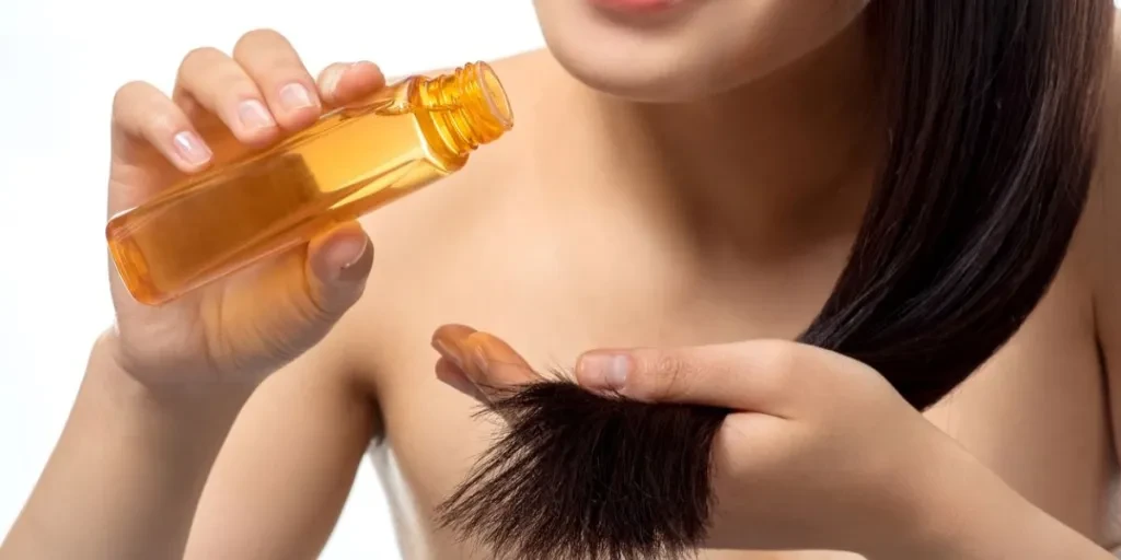 cropped shot of smiling woman pouring oil on split ends isolated on white