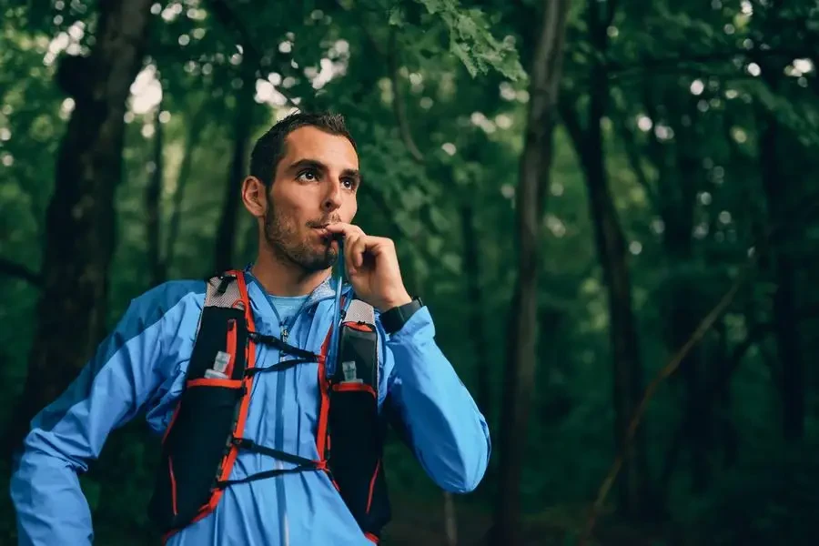 it male jogger hydrates during day training for cross country forest trail race in nature park