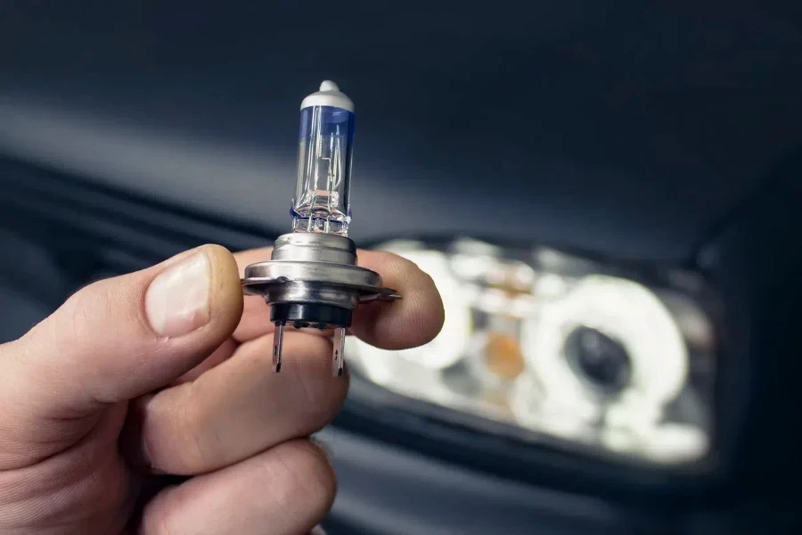 Man holds in his hand a halogen light bulb against the background of the headlights on