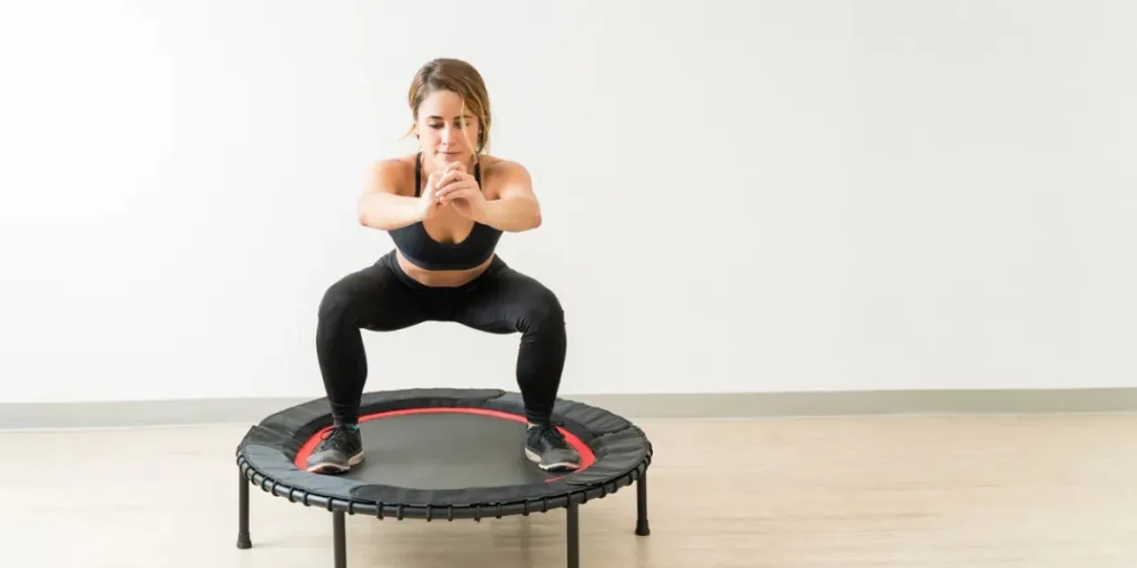 jolie jeune femme brune faisant du trampoline tout en faisant des squats contre le mur au studio pendant un entraînement de fitness