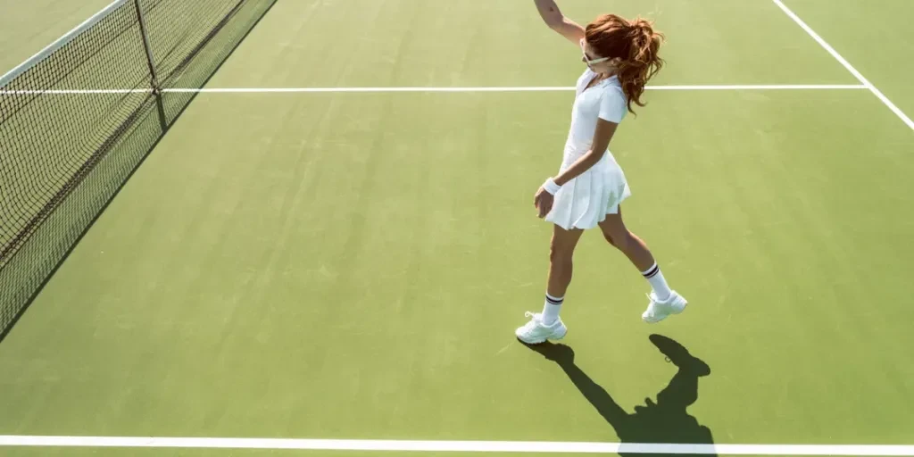 side view of young attractive woman in white tennis uniform playing tennis on court