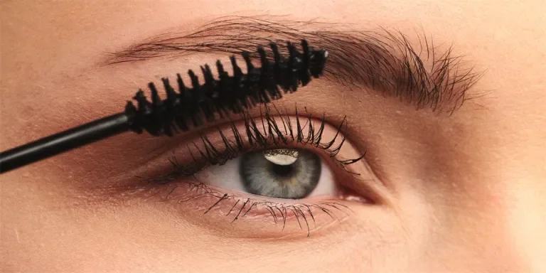 stylist applies black mascara on the eyelashes of the female eye
