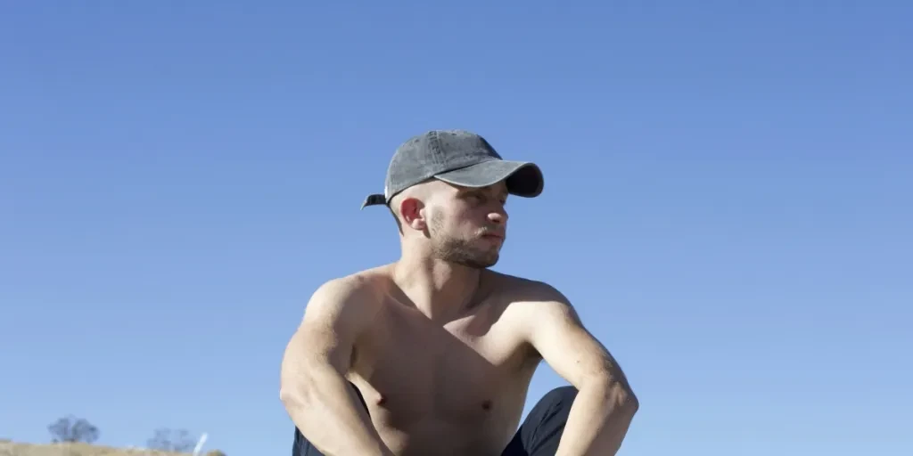 topless man in blue denim jeans and brown cowboy hat sitting on black car during daytime