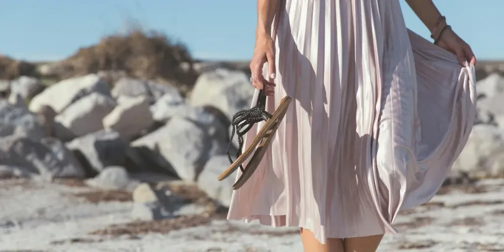 woman wearing white skirt holding black leather flat sandals standing