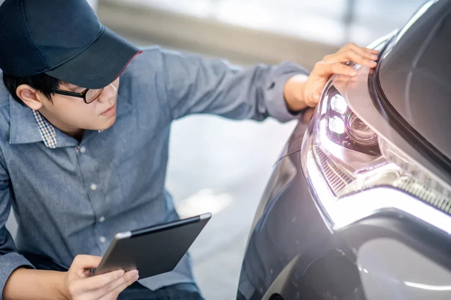 Young Asian auto mechanic holding digital tablet checking headlight in auto service garage