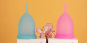 Blue and pink menstrual cups on a yellow background with a flower accent. Ideal for modern health concepts