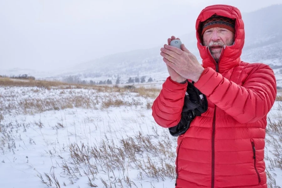 Cold Senior Male Hiker with a Pocket Electric Hand Warmer