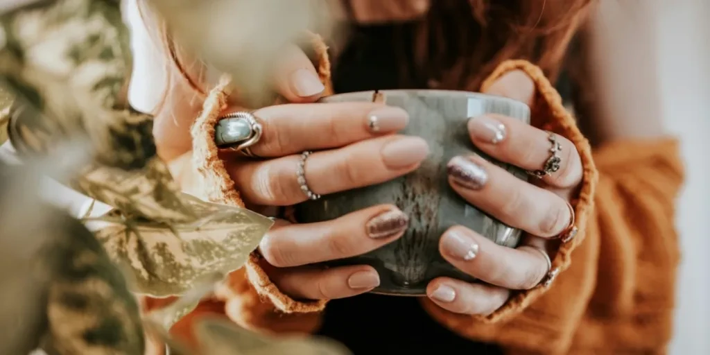 Person holding a cup with fall nail colors