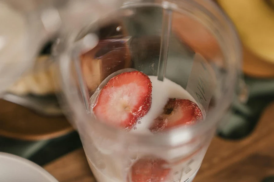 Sliced strawberries immersed in milk inside a blender, ready for a healthy smoothie preparation