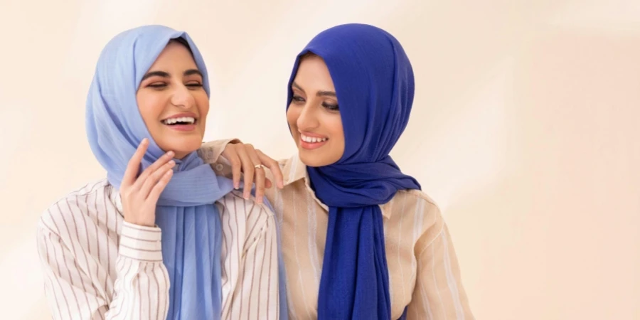 Dua Wanita Tersenyum dengan Hijab Warna-warni di Latar Belakang Netral