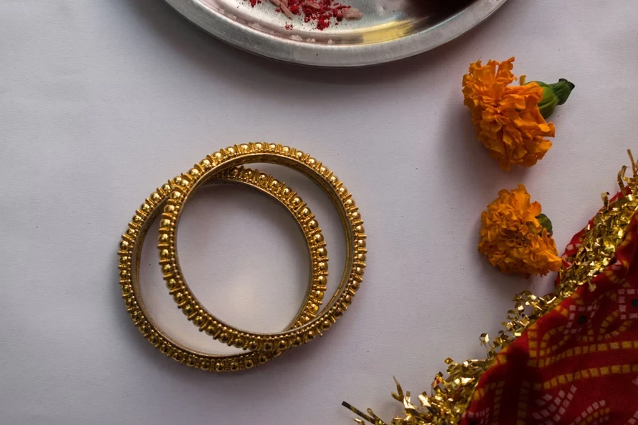 Two opulent gold bracelets next to flowers on a table