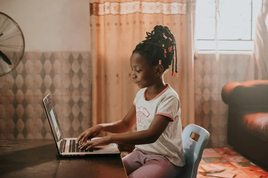 A child sitting at a desk using a laptop in a warmly lit room, showcasing modern technology and learning