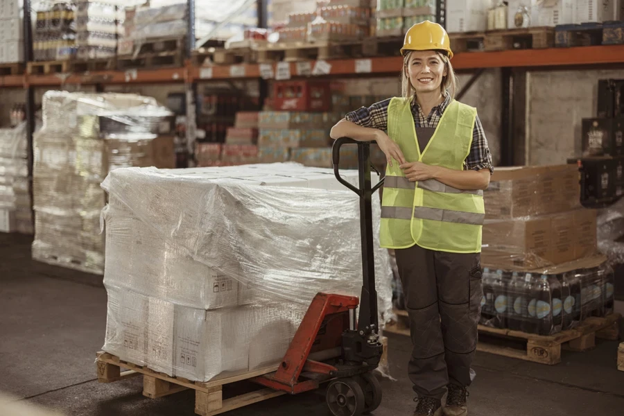 A smiling female worker standing next to a pallet truck