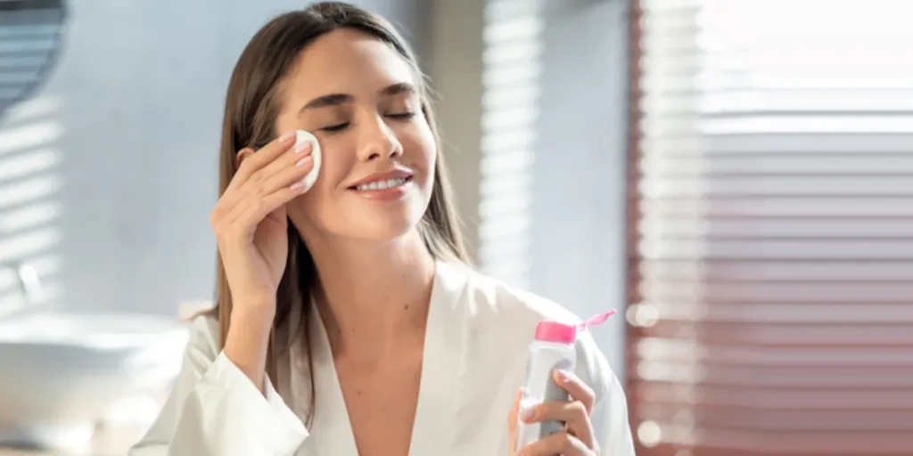 A smiling woman using a face cleanser