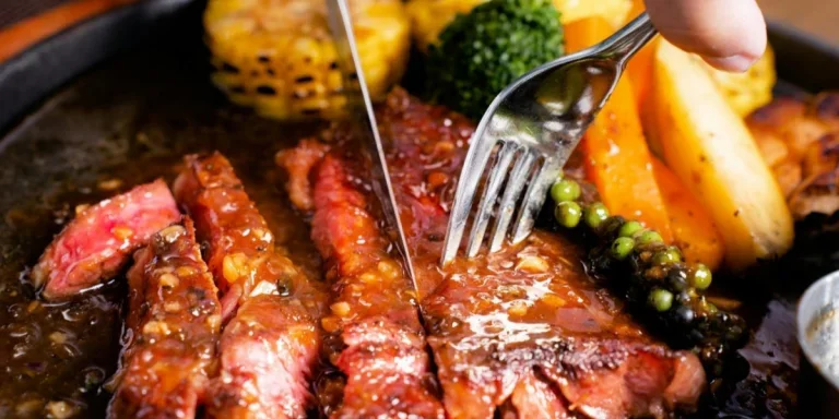 A steak knife slicing through steak served on a plate