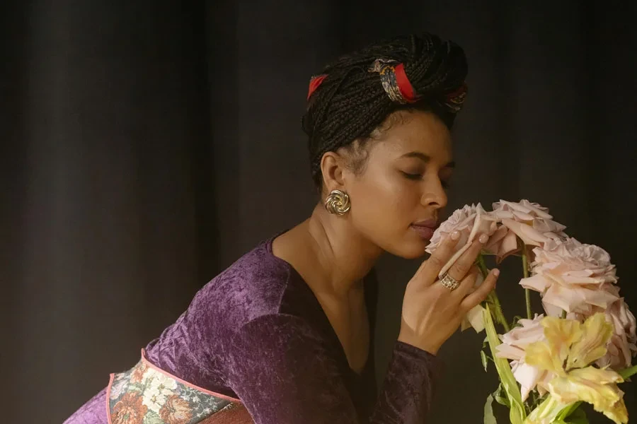 A woman in a velvet dress posing with closed eyes, holding pink roses in a studio setting