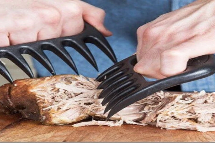 Black plastic meat claws pulling apart seasoned chicken