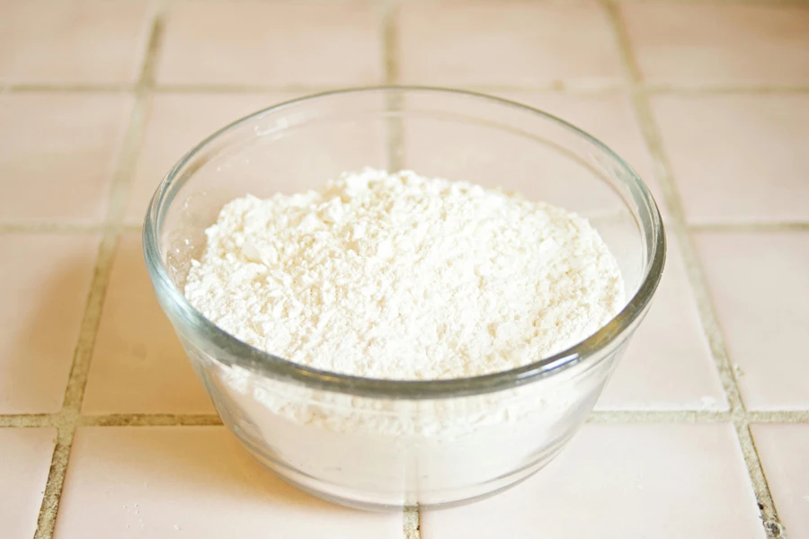 Close-up of a clear glass bowl containing flour on a tiled kitchen counter