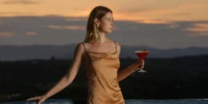 Fashionable young woman holding a cocktail on beautiful sunset background