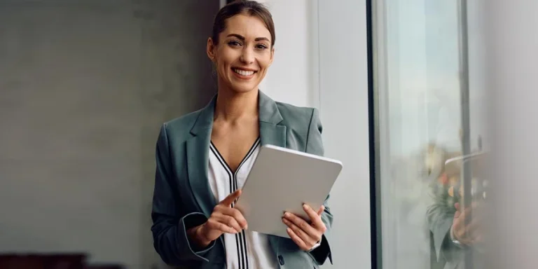 Happy female entrepreneur using touchpad while working in the office and looking at camera