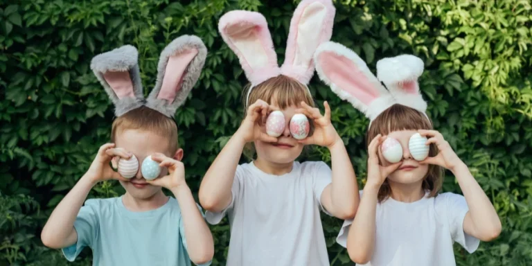 Smiling children wearing a headband with bunny ears found Easter eggs in the garden and brought them to their eyes. Siblings celebrate Easter. Religious holiday concept