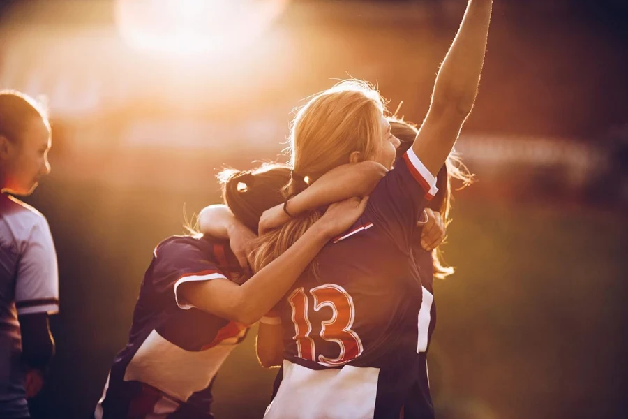 Ein Team glücklicher Fußballerinnen feiert seinen Erfolg bei Sonnenuntergang auf einem Spielfeld.