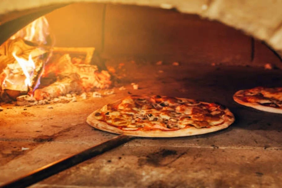 Two thin crust pizzas baking inside stone pizza oven