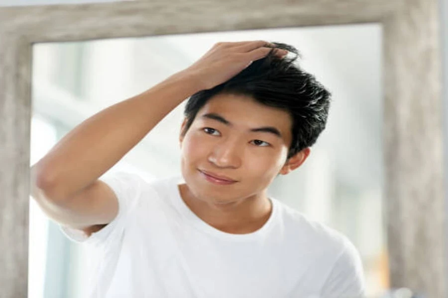 Young man fixing gelled hair in mirror at home