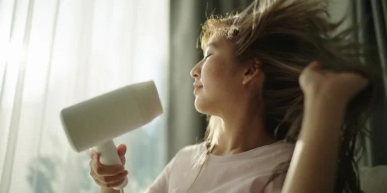 Молодая женщина сушит волосы феном