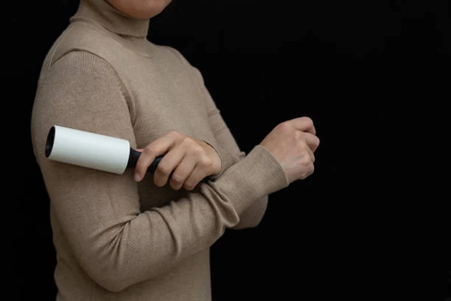 Mujer joven usando un quitapelusas o un rodillo adhesivo para limpiar su suéter. Aislado sobre fondo negro.