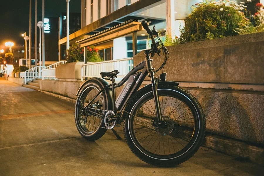 A bicycle is parked on a city street at night, surrounded by modern architecture and plants