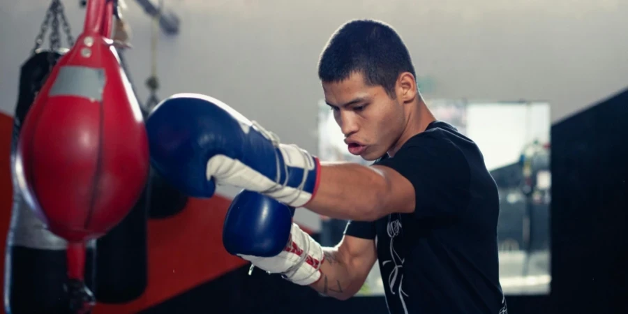 A determined boxer trains with a punching bag in a boxing gym, wearing gloves and sportswear