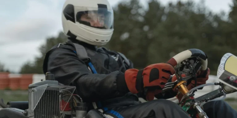 A focused go-kart racer in full gear steering on an outdoor track