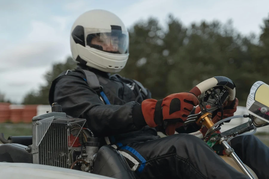 A focused go-kart racer in full gear steering on an outdoor track