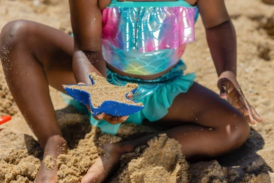 A kid in fancy swimwear seated on the sand