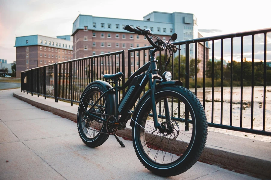 A modern electric bike parked beside a metal railing on a city sidewalk at dusk