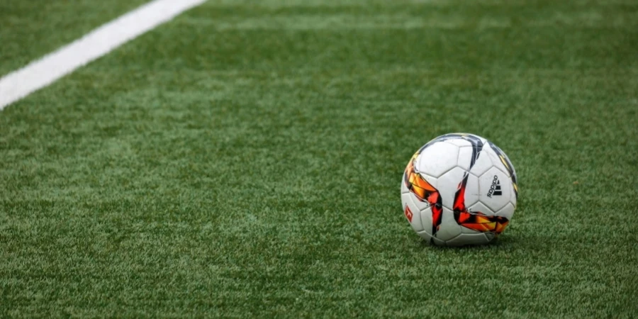 A vibrant soccer ball resting on a pristine grass field beside a white sideline