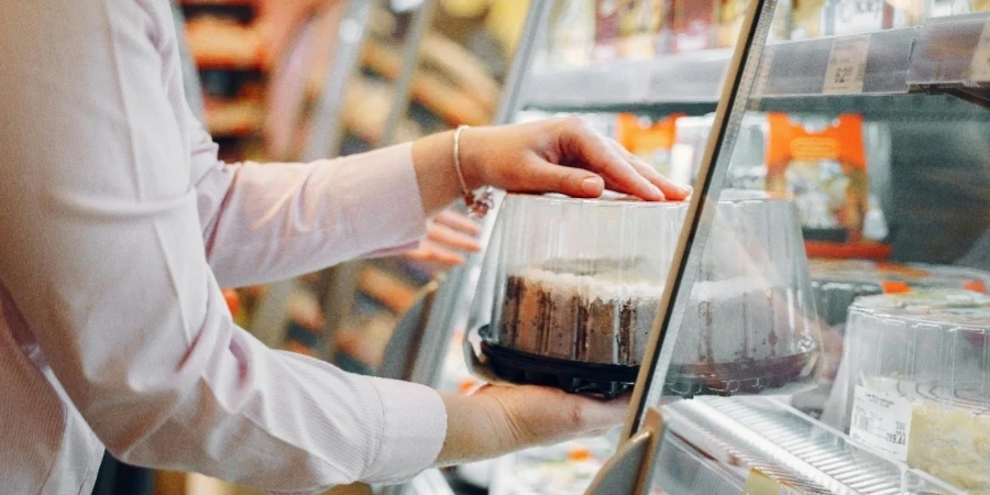 A woman choosing a packaged cake from a supermarket chiller
