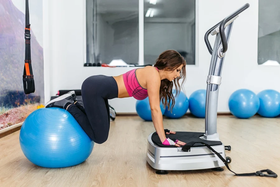 A woman training with a vibrating plate and fitness ball.