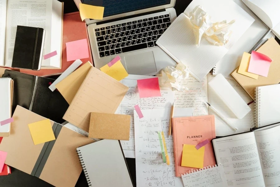 Above view of a laptop surrounded by notebooks and paper