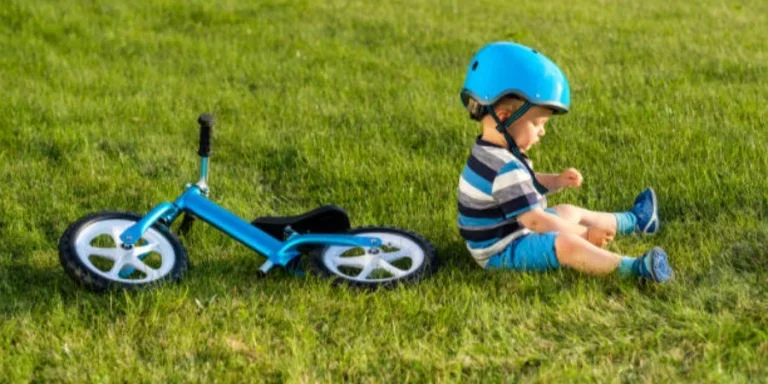 Boy in Helmet Sitting on Grass with Blue Balance Bike