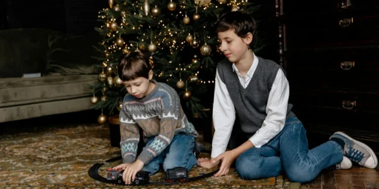 Мальчики играют с игрушечным поездом под рождественской елкой
